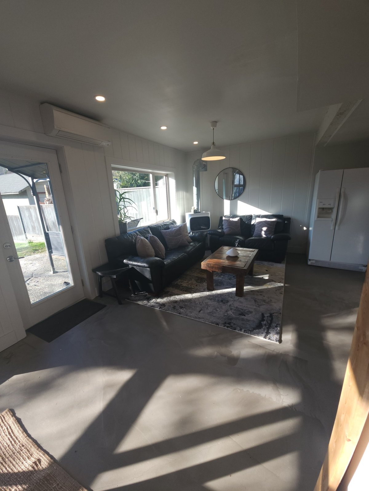 Modern living room with black sofa, wooden coffee table, and large windows letting in natural sunlight, minimalist interior design