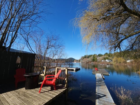 Red Adirondack chair on a wooden dock overlooking a calm lake with forested shore and clear blue sky