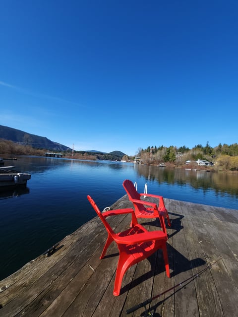 Bright red Adirondack chairs on a wooden dock overlooking a calm blue lake with mountains and forested shores
