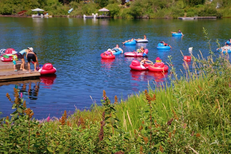 Group of people in red and blue kayaks on a calm river surrounded by lush green vegetation and riverside homes