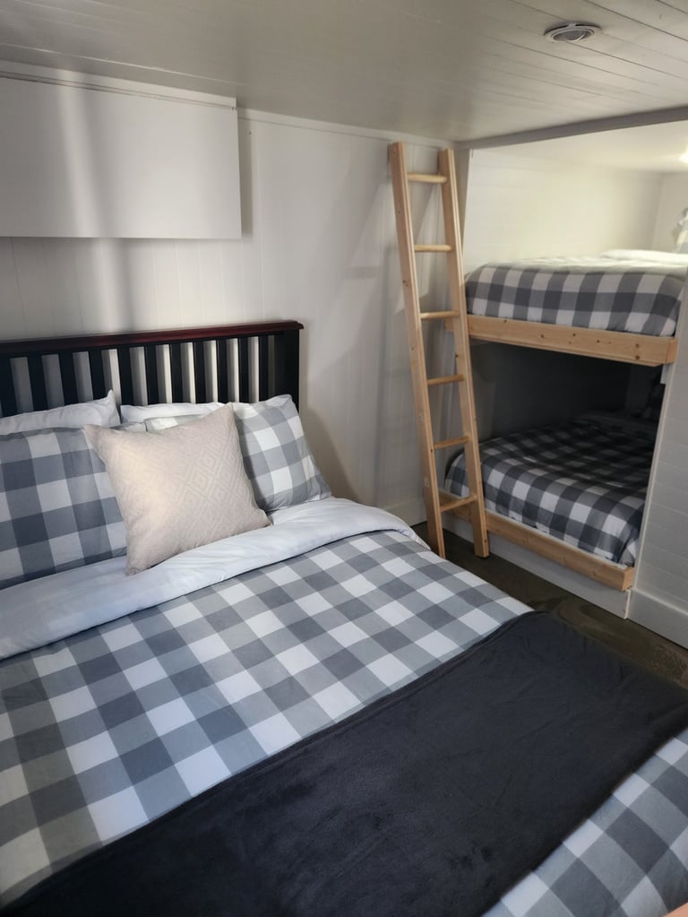 A cozy bedroom with a queen bed featuring gray and white checkered bedding and a wooden bunk bed with matching linens against white walls